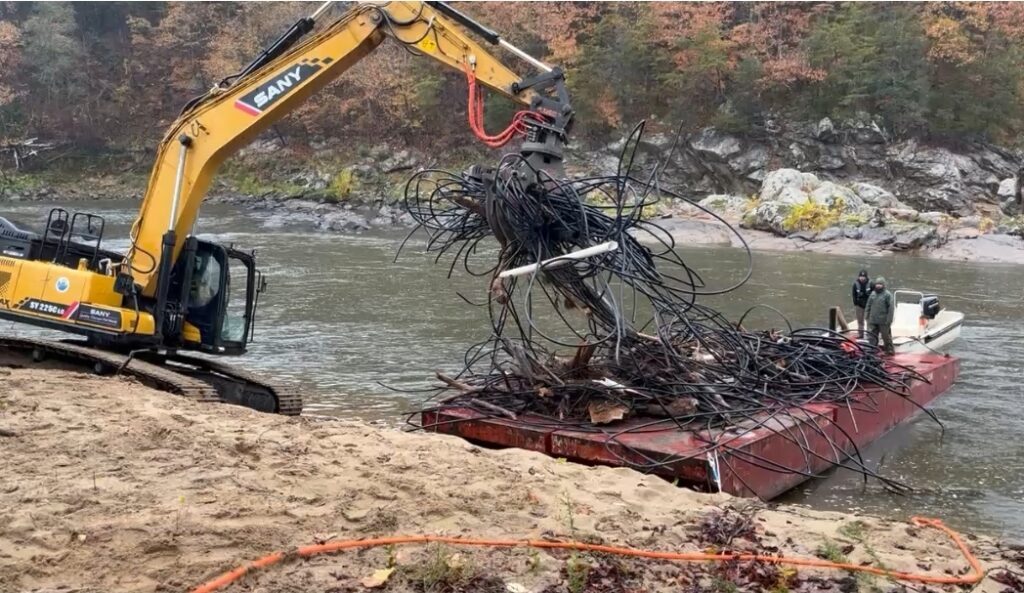 Excavator moves pipe onto a barge sitting on the French Broad River