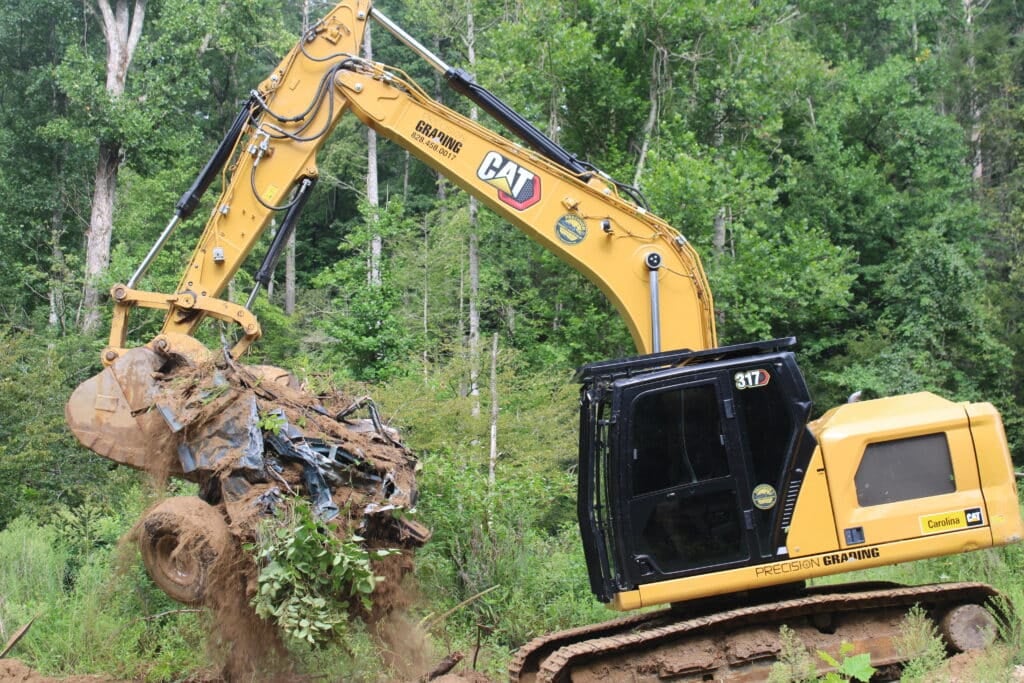 Precision Grading's excavator pulls a mangled car from the banks of the Big Hungry River. Photo by Liz McGuirl